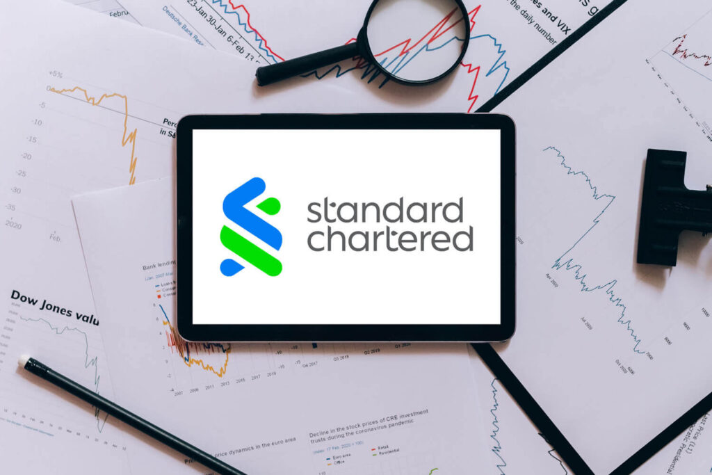 An iPad displaying the Standard Chartered logo surrounded by charts and graphs