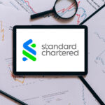 An iPad displaying the Standard Chartered logo surrounded by charts and graphs