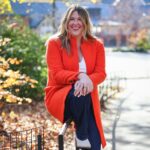 A professional portrait of Katy Foucar-Szocki, the senior director of Unboxed Training & Technology. She is sitting against a park fence in autumn, wearing a highly saturated red coat.