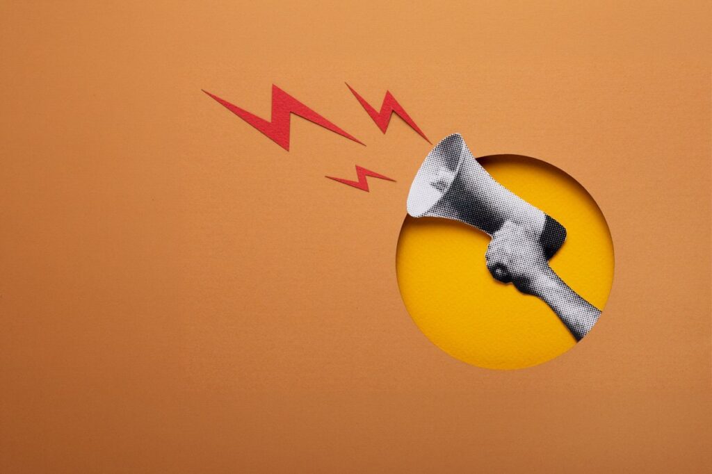 A paper-cut art style illustration of a hand holding a megaphone with red lightning bolts, representing powerful communication to overcome market research challenges