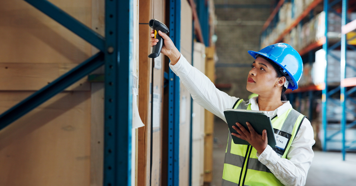 warehouse professional in a blue hard hat using a hand scanner and tablet to manage supplier traceability and overcome manufacturing challenges