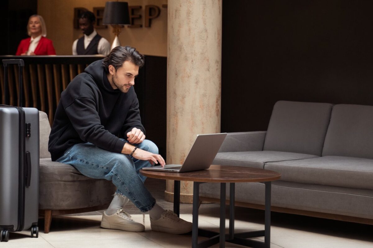 A modern traveler working on a laptop in a hotel lobby, illustrating how hybrid work influences current travel demand trends.