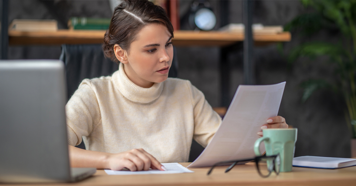 A professional woman at a desk reviewing printed documents and a laptop, highlighting the focus required to overcome qualitative market research challenges in multiple languages.