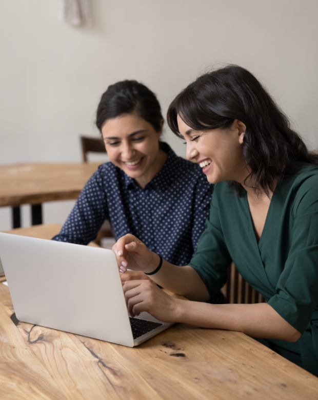 Two women sharing a laugh while working together on a laptop, highlighting collaborative Creole translation services