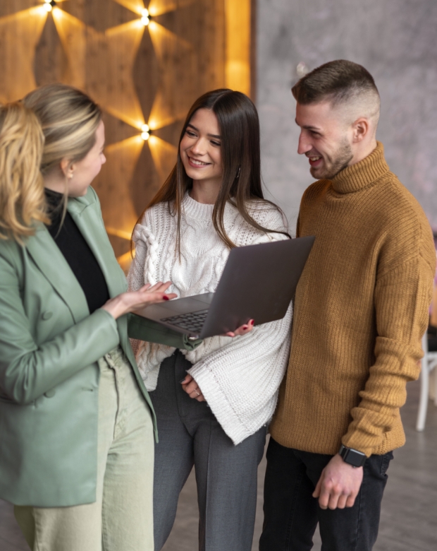 Three young professional colleagues smiling and discussing a project on a laptop in a modern office, representing Flemish language translation and business services