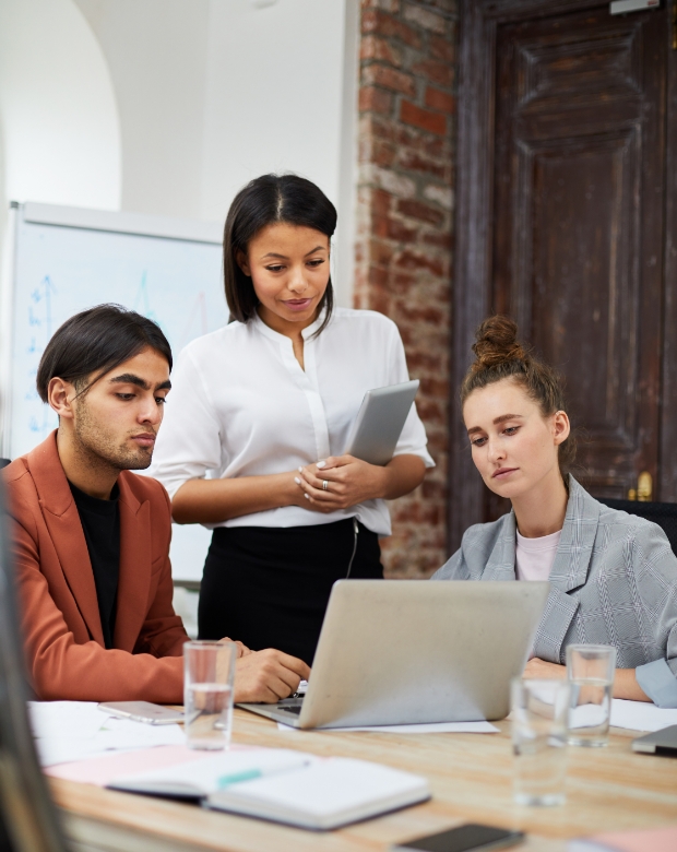 Three professional colleagues collaborating in a rustic office, reviewing data on a laptop and holding a tablet, representing Simplified Chinese translation and business services
