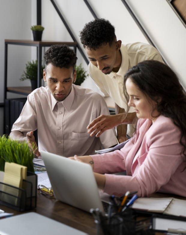 Three professionals gathered around a desk reviewing documents and a laptop together, representing Tamil translation and business communication