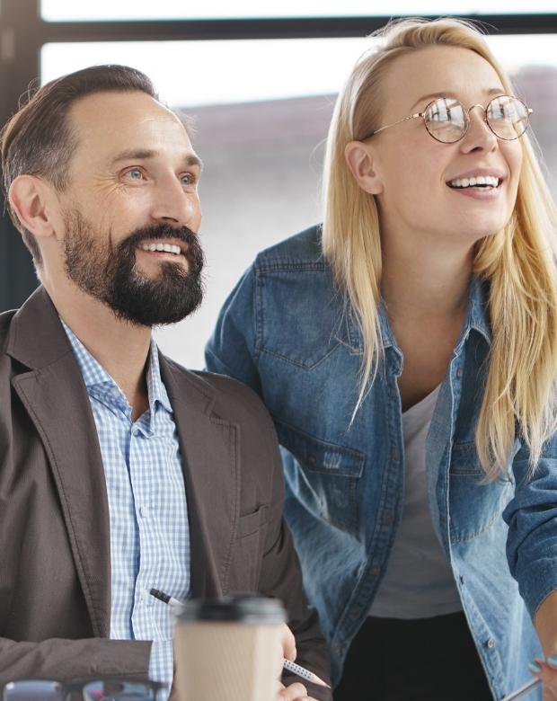 A professional man and woman smiling while looking toward a shared screen, representing expert Welsh translation and linguistic support