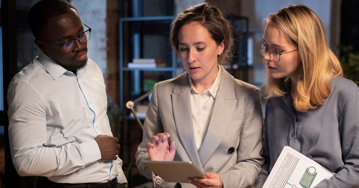 Three legal professionals gathered around a tablet reviewing documents together, showing human collaboration in a legal team