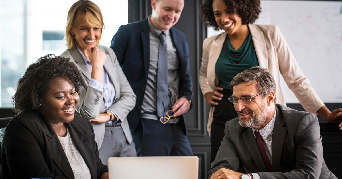 A diverse team of legal professionals smiling and collaborating around a laptop, representing the human and AI partnership in legal work