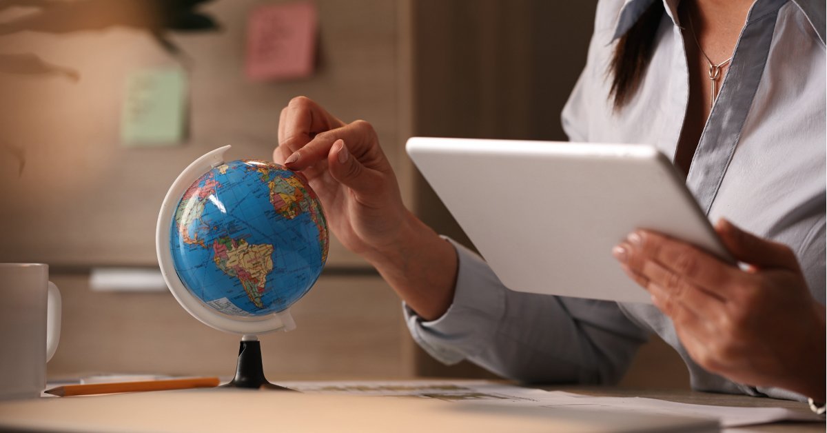 Woman holding a tablet and pointing at a globe on a desk, representing the growth of global market research across international markets
