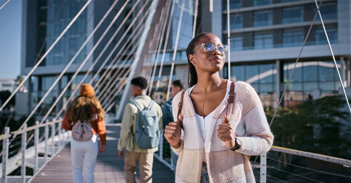 A young woman with a backpack crosses a modern bridge in an urban setting, representing how the luxury traveler profile has shifted as part of current trends in travel and tourism.
