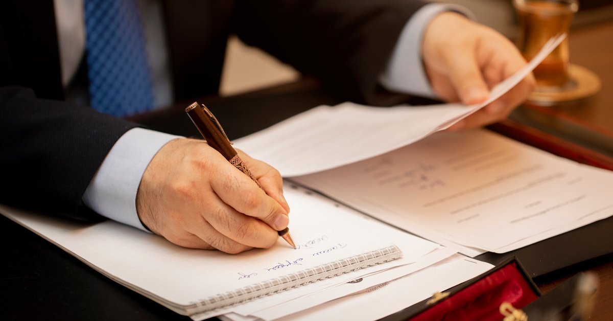A lawyer signing legal documents by hand while reviewing paperwork, illustrating the importance of human oversight in legal document review