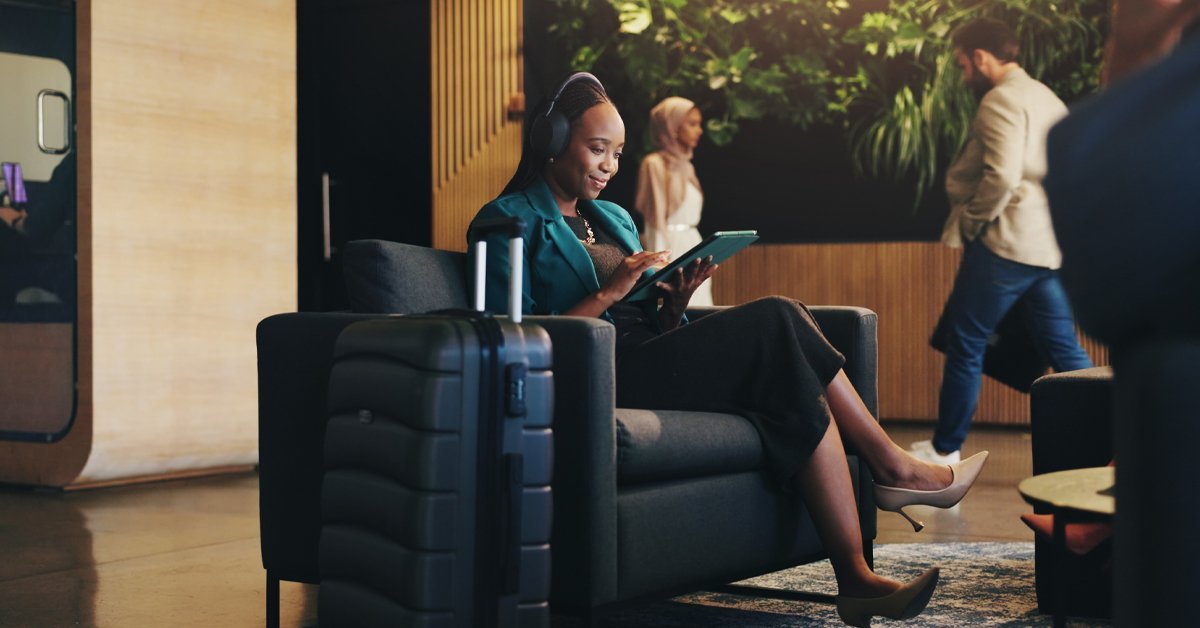 A business traveler sits in a hotel lobby with luggage, using a tablet, showing how personalization and language quality shape the guest experience amid current trends in travel and tourism.