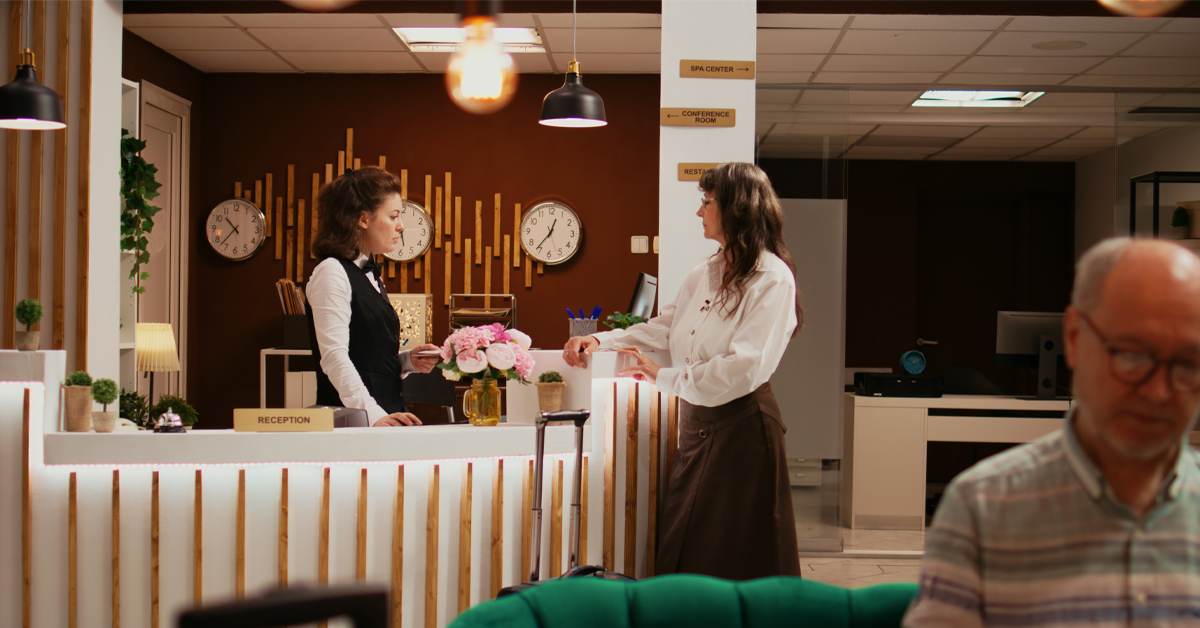A hotel receptionist checks in a guest at a front desk, illustrating what current trends in travel and tourism mean for brand voice and the multilingual guest experience.