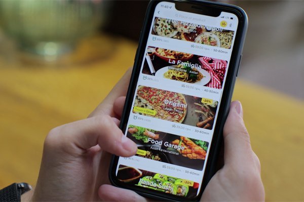 A person browsing a multilingual food delivery app on a smartphone showing restaurant listings in multiple languages