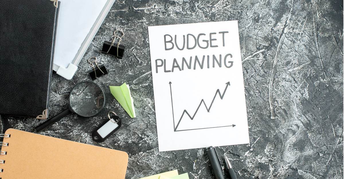 A handwritten "Budget Planning" note with an upward trend graph, surrounded by office supplies
