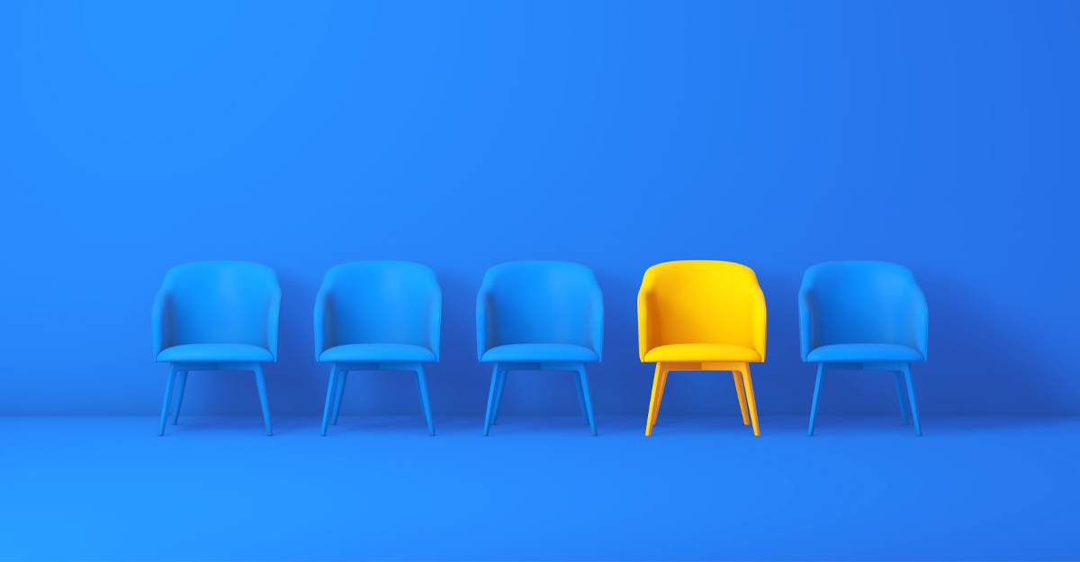 A single yellow chair standing out among a row of blue chairs